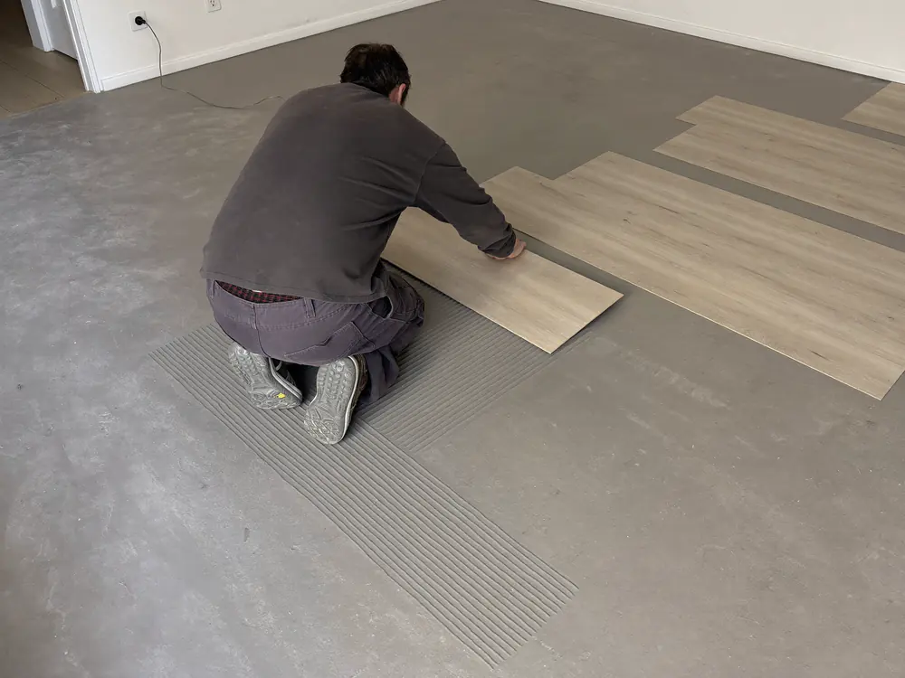Vloerlegger drukt een plak-PVC plank aan op een geegaliseerde ondergrond