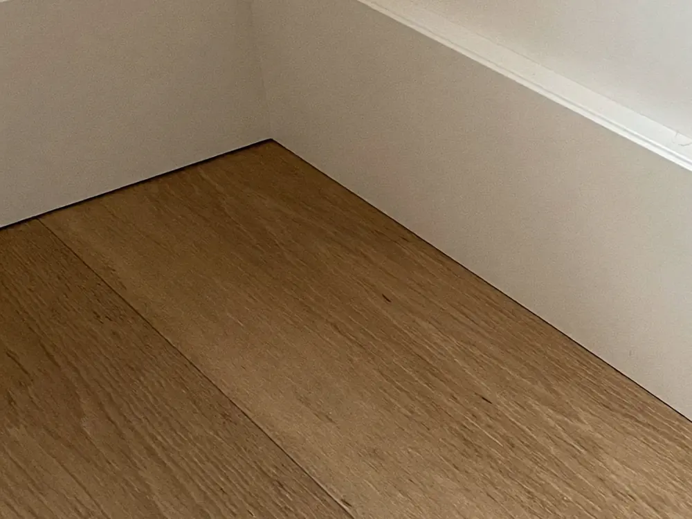 Witte plinten in een strakke binnenhoek op een nieuwe eikenlook PVC vloer
